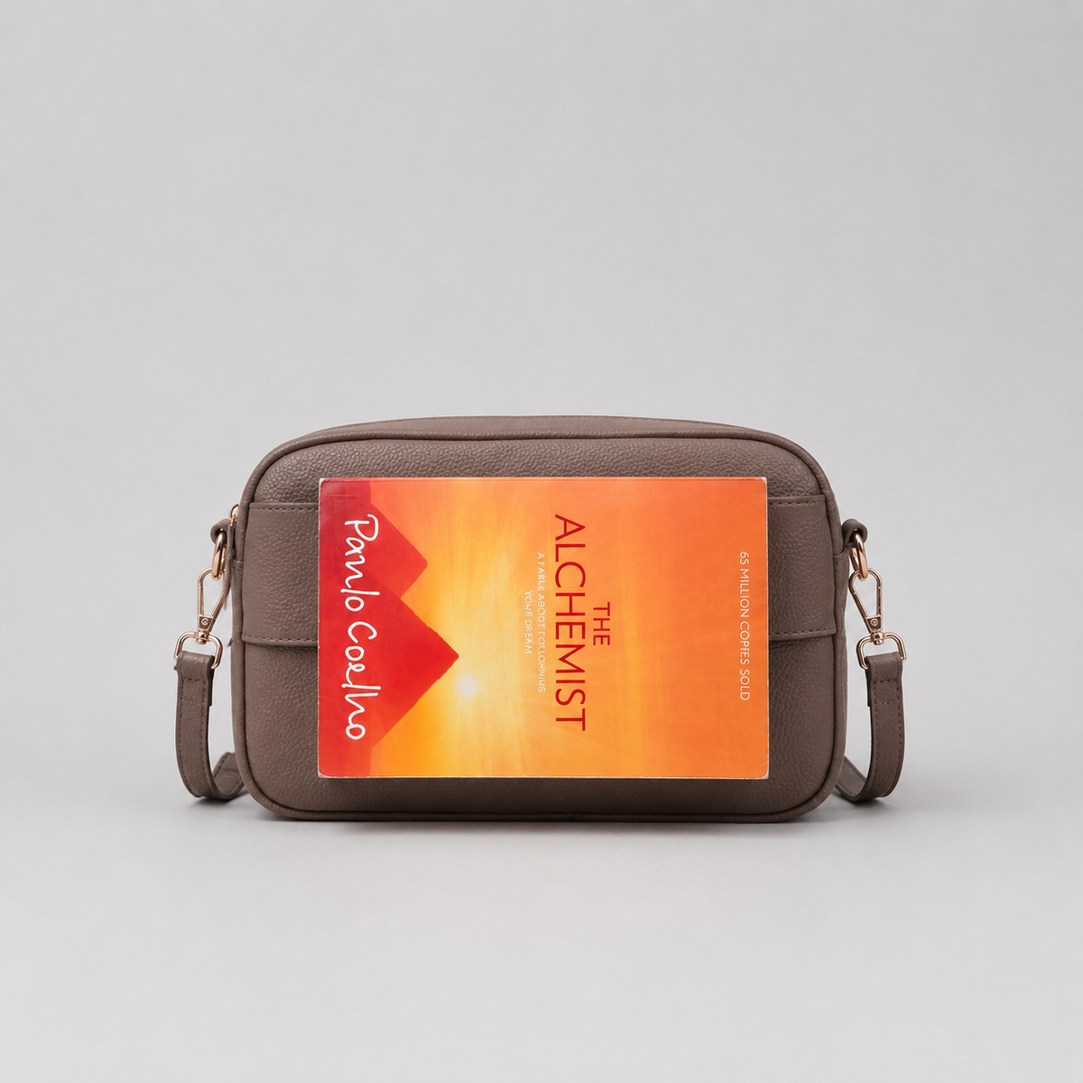 The Daily Taupe Brown bookmark-inspired crossbody bag holding a book