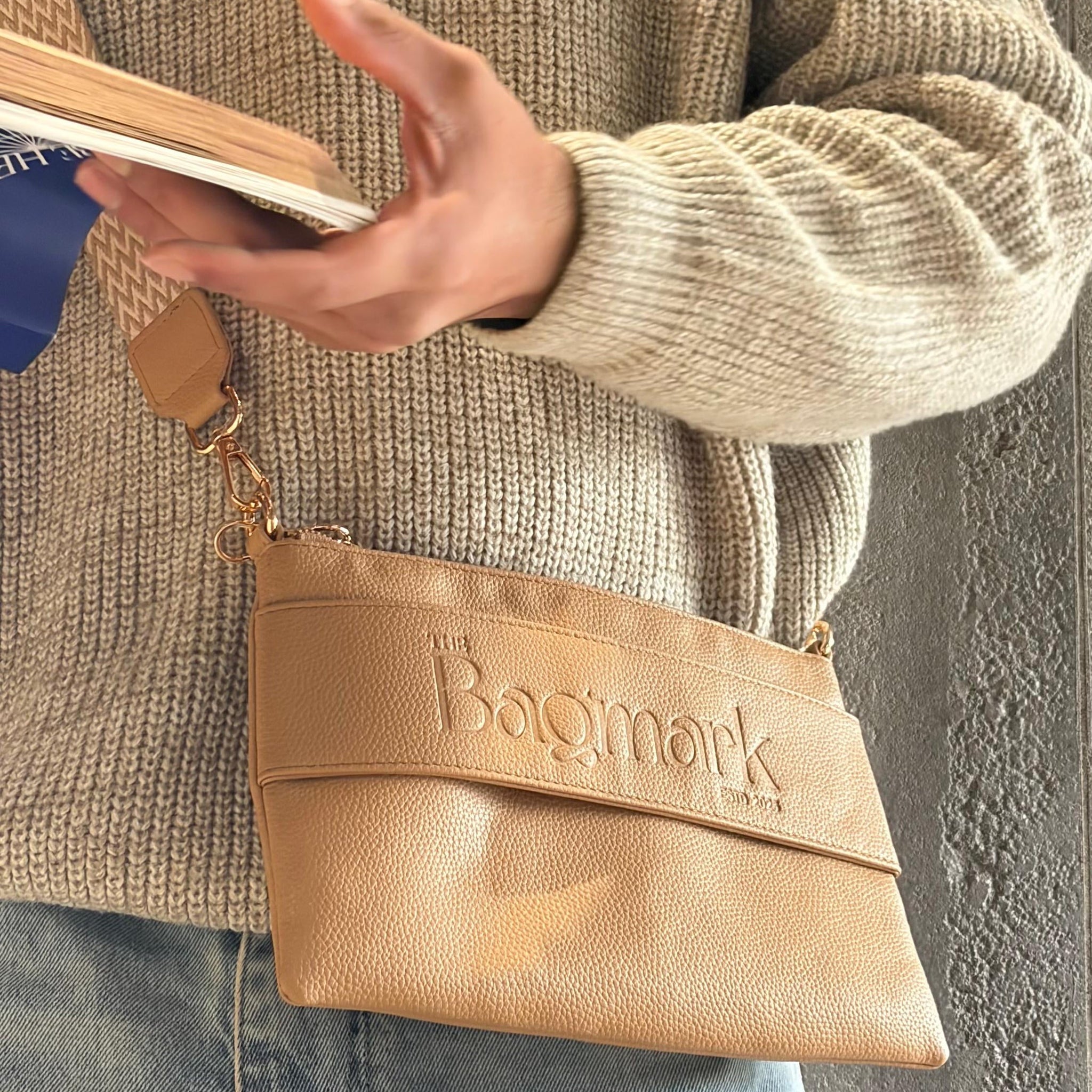 The Essential Camel bookmark-inspired crossbody bag holding a book in a bookstore